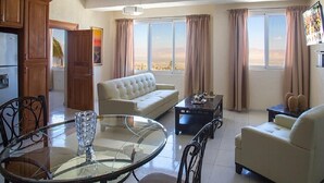 A living room with a sofa, armchairs, a glass coffee table, and a dining table with chairs. - Residences Talou (Petionville)