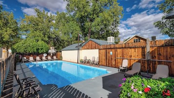 A swimming pool with lounge chairs, a wooden fence, and a house in the background.