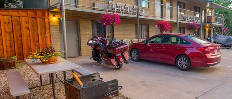 Ein zweistöckiges Motel mit überdachtem Parkplatz, einem Grill und einem roten Auto davor.