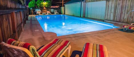 A backyard with a swimming pool, lounge chairs, and a wooden fence.