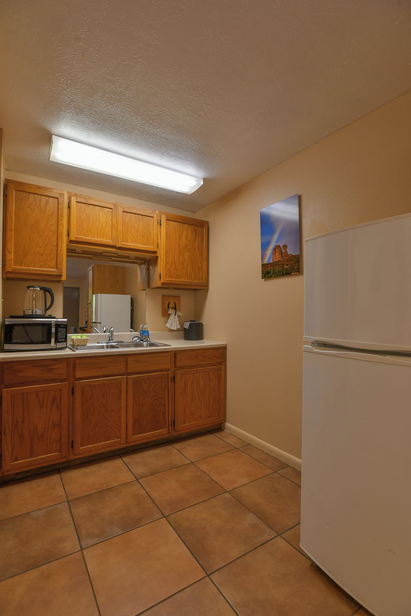 A kitchen with wooden cabinets, a microwave, a sink, and a refrigerator.