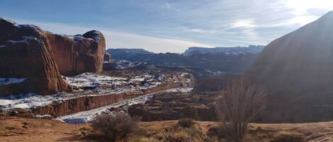 A rugged canyon landscape with a road cutting through it, surrounded by rocky formations and sparse vegetation.