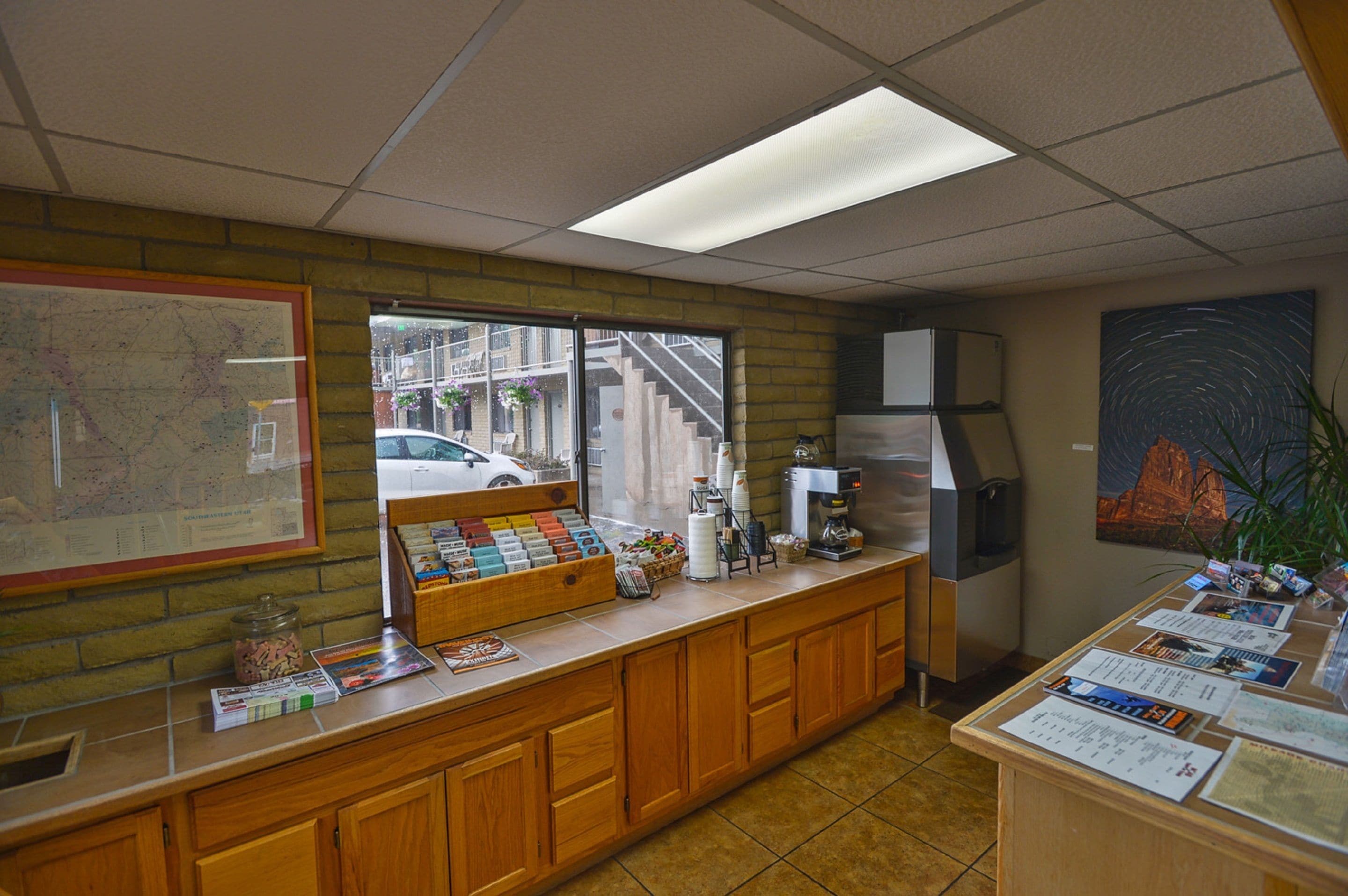 A reception area with a wooden counter, a coffee machine, a map on the wall, and a window with a view of the street.