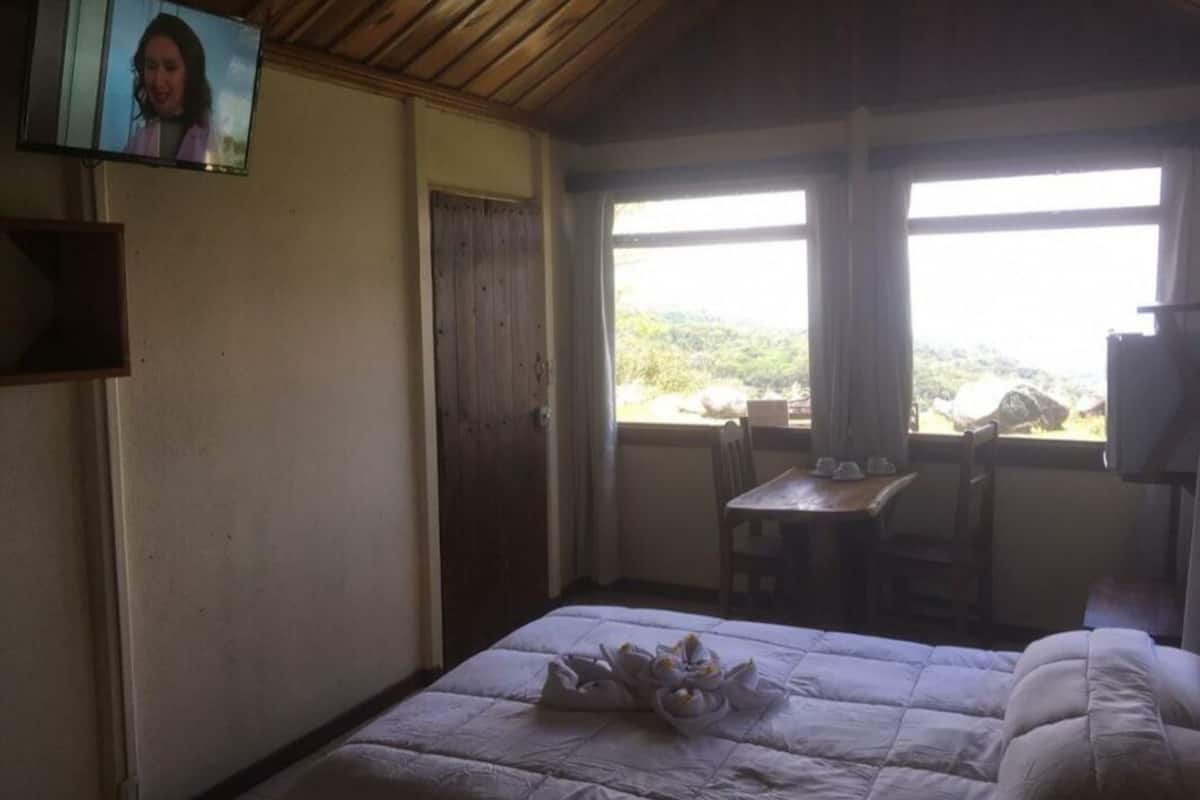 A room with a bed, a table, and a TV mounted on the wall.