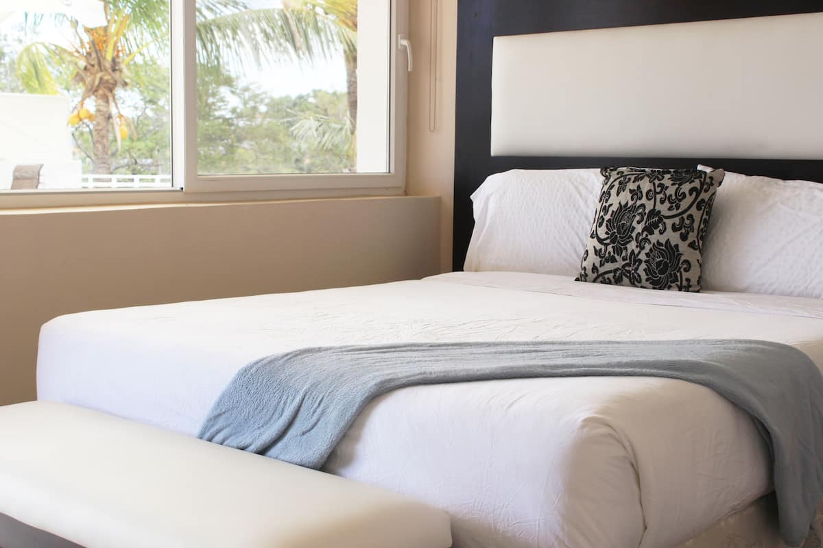 A bed with white bedding, a grey throw blanket, and a black and white patterned pillow.