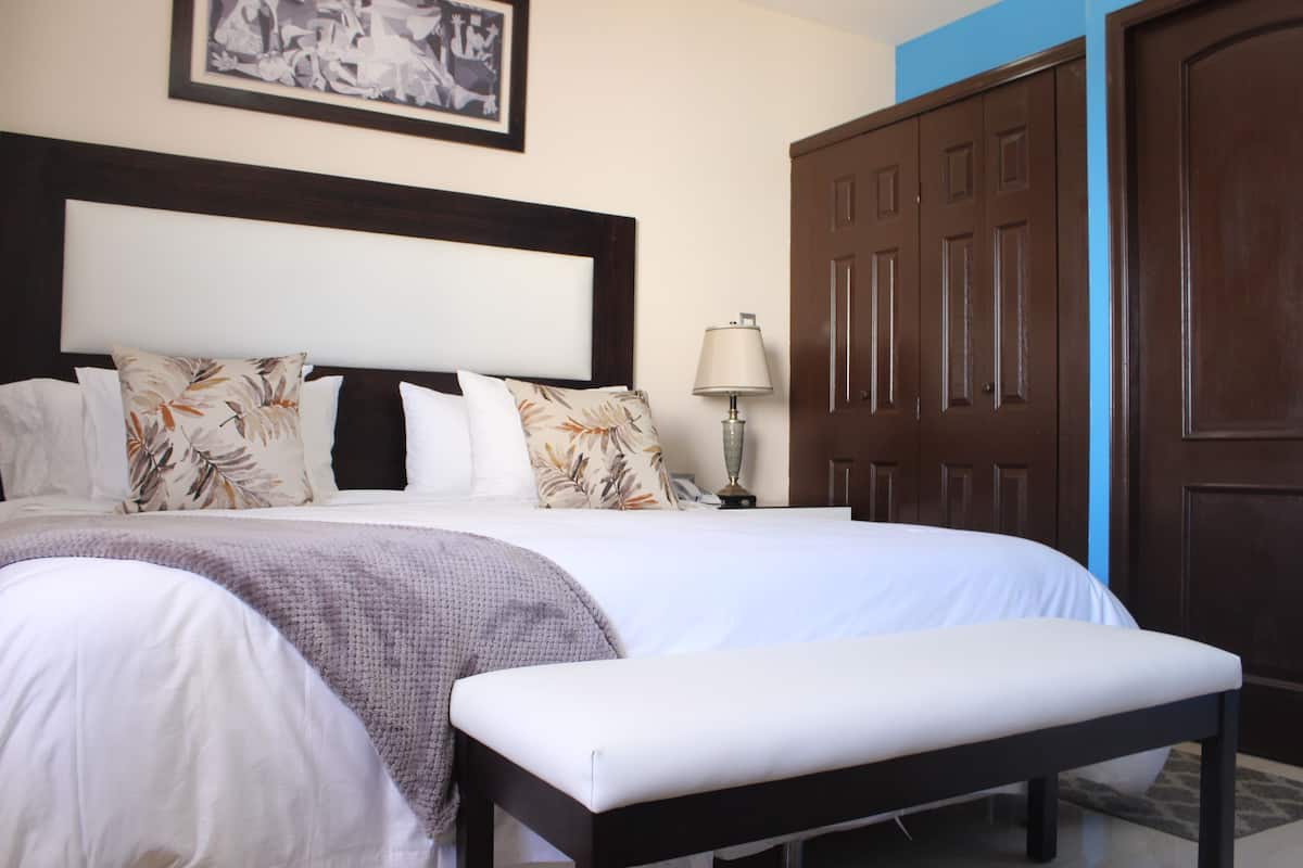 A neatly made bed with a headboard, a bedside lamp, and a large wooden wardrobe.