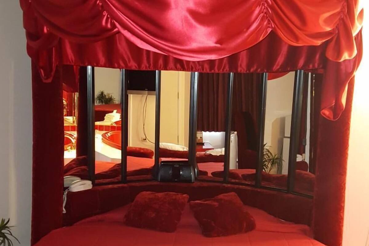 Un grand lit doté d’un baldaquin rouge et agrémenté d’une décoration en forme de cœur faite avec des serviettes.