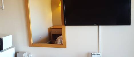A hotel room with a wooden dresser, a flat-screen TV mounted on the wall, a mirror, a telephone, and a small table with toiletries.