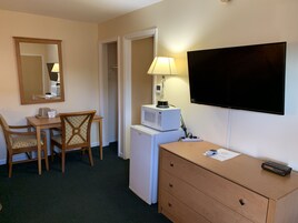 Una habitación de hotel con escritorio, silla, microondas, televisor y cómoda.