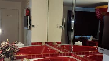 A bathroom with a red bathtub, a large mirror, and a white towel rack.