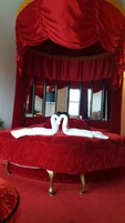 Una cama con dosal rojo y dos almohadas con forma de cisne.