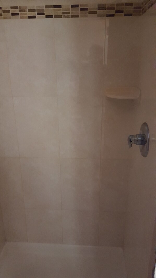 A bathroom with beige tiles, a showerhead, and a small shelf. - New Relax INN (Bridgeview)