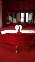 Una cama con ropa de cama roja y dos toallas blancas dispuestas en forma de cisnes.