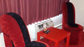 A room with two red velvet armchairs, a small red table, and a window with red curtains.