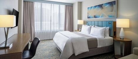 A hotel room with a large bed, a desk, a chair, a TV, and a window with curtains.