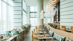 A modern restaurant with high ceilings, large windows, and a mix of seating arrangements including tables and booths. - The Westin Sarasota (Sarasota)