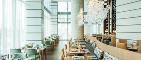 A modern restaurant with high ceilings, large windows, and a mix of seating arrangements including tables and booths.