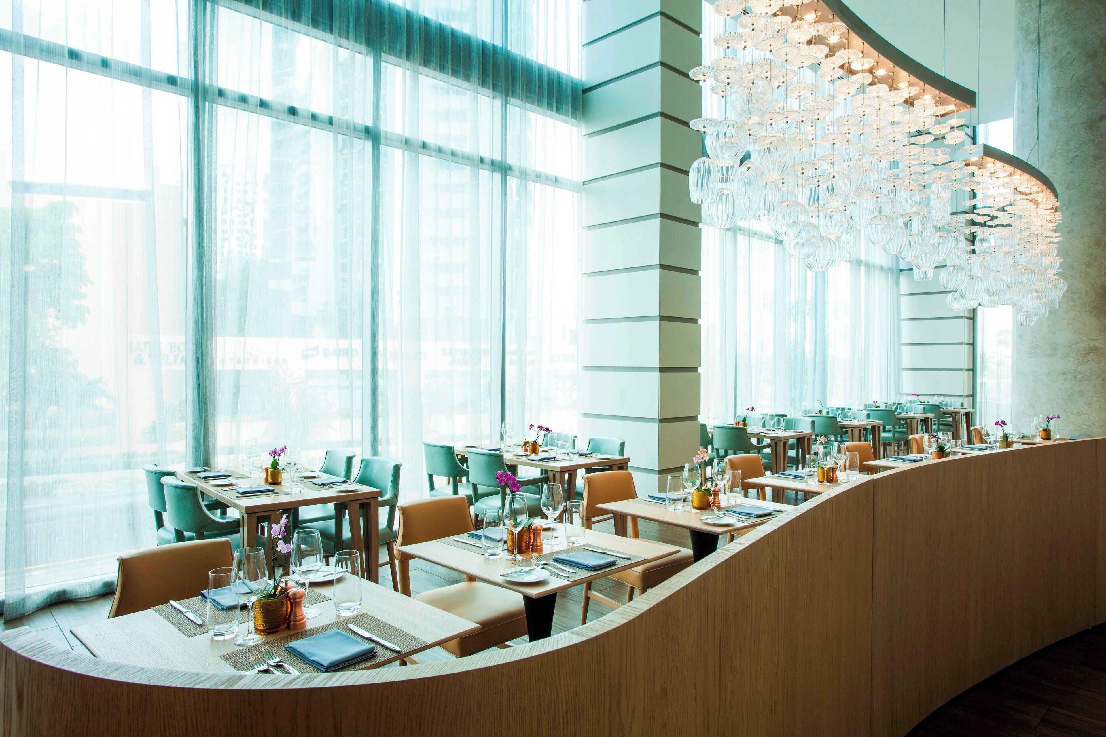 Ein modernes Restaurant mit einer gebogenen Theke, großen Fenstern und einer dekorativen Kristallleuchtre.'