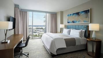 A hotel room with a large bed, a desk, a chair, a TV, two lamps, and a painting.