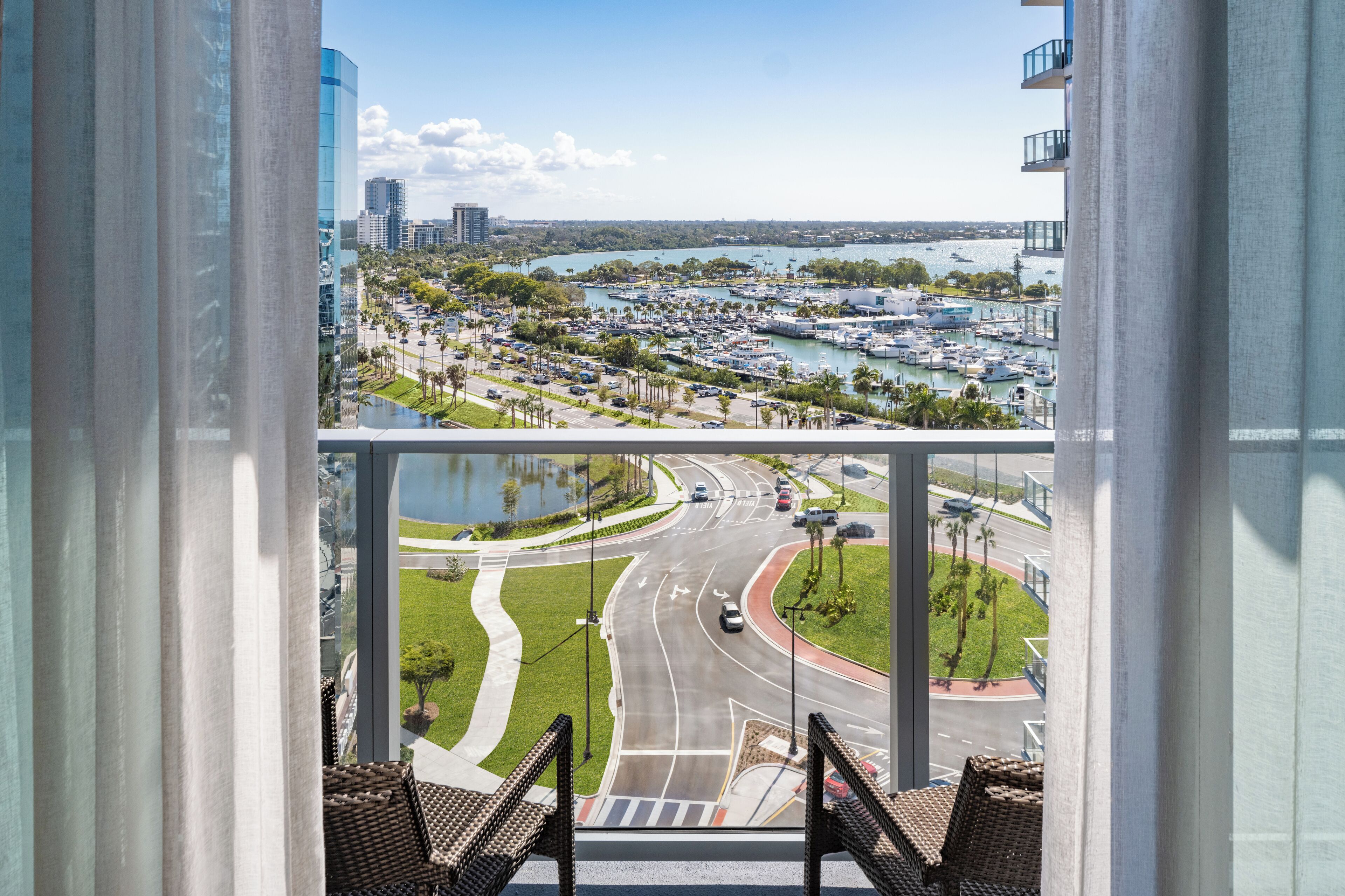A view from a balcony overlooking a marina with boats, a road with cars, and a river.