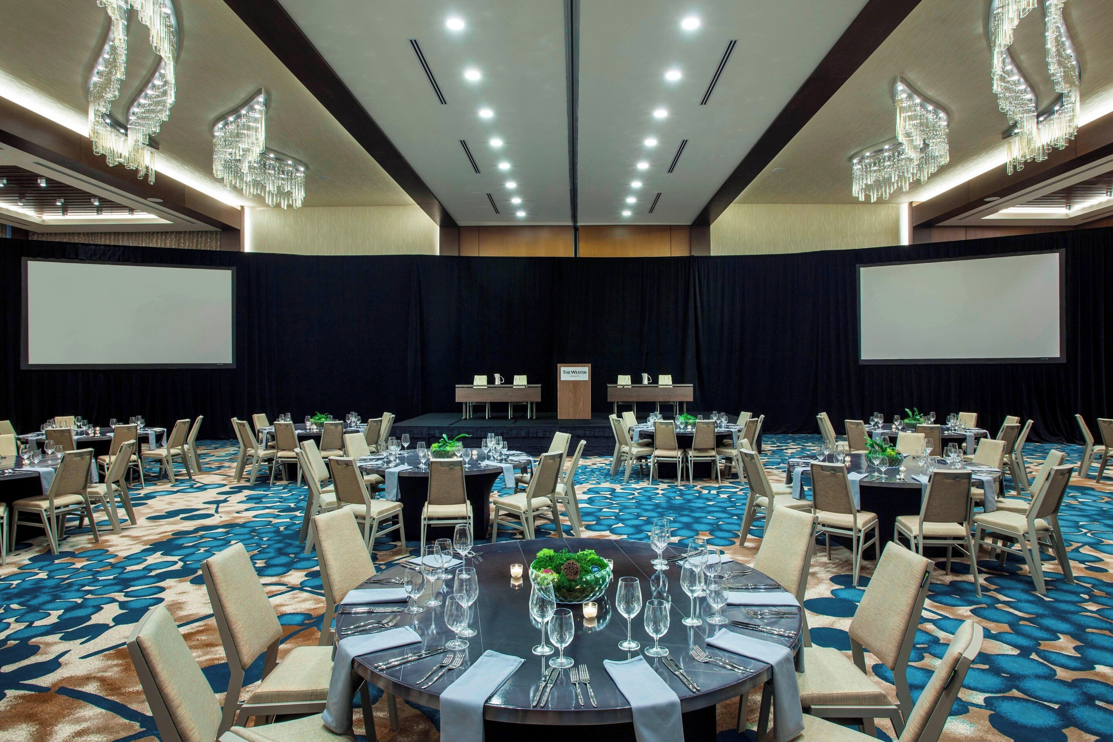 A conference room with round tables, chairs, and a stage with a screen.