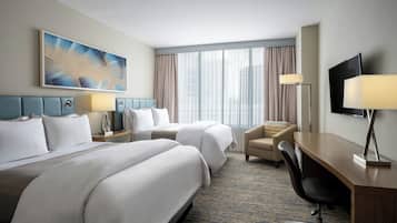 A hotel room with two beds, a desk, a chair, a TV, and a large window with curtains.