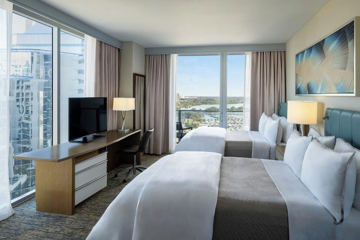 Ein Hotelzimmer mit einem großen Bett, einem Schreibtisch mit Fernseher und Blick auf eine Stadtlandschaft.