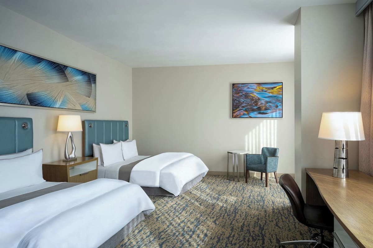 Ein Hotelzimmer mit zwei Betten, einem Schreibtisch, einem Stuhl und Bildern an den Wänden.
