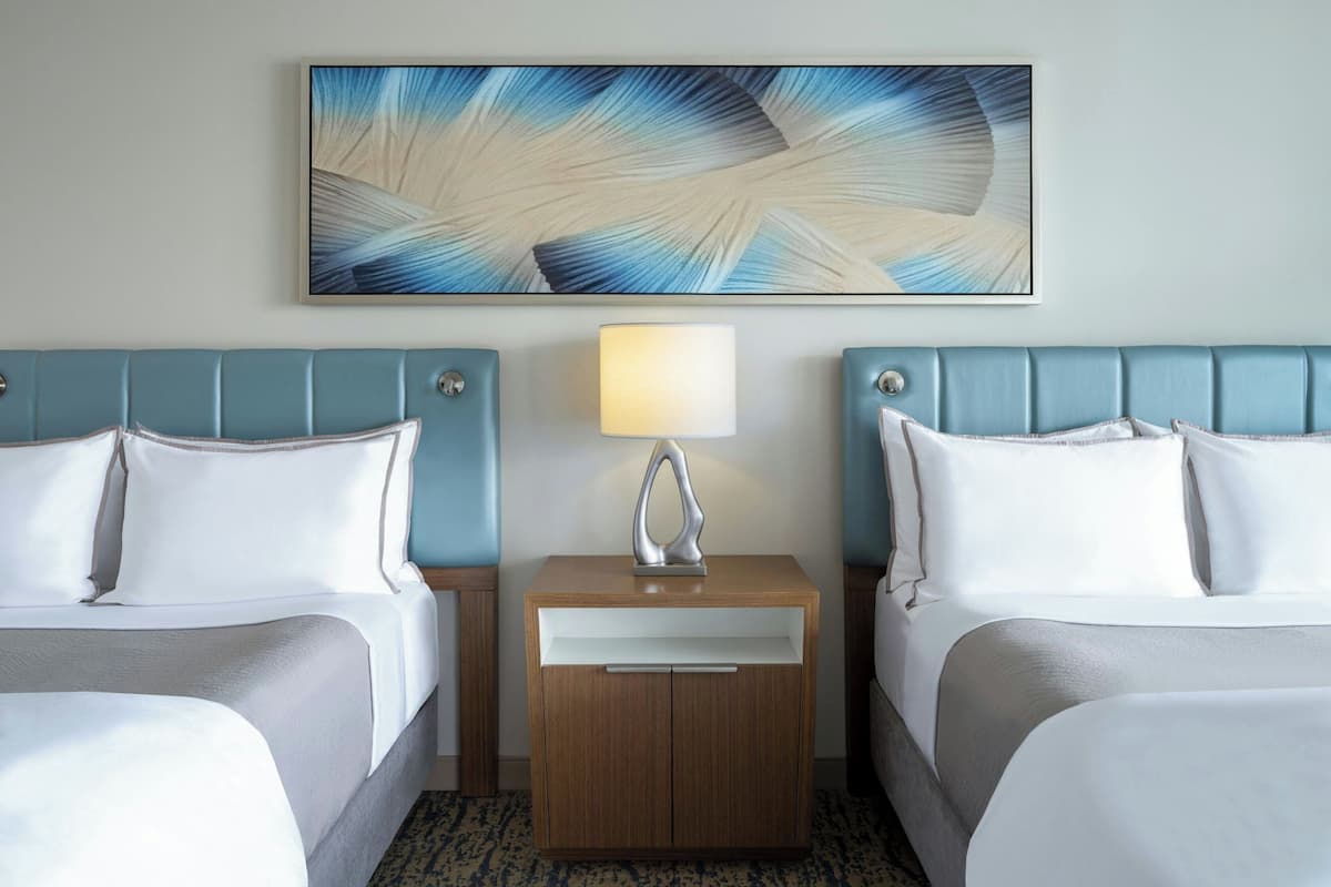 Ein Hotelzimmer mit zwei Betten, einem Nachttisch mit Lampe und einem großen, abstrakten Gemälde an der Wand.