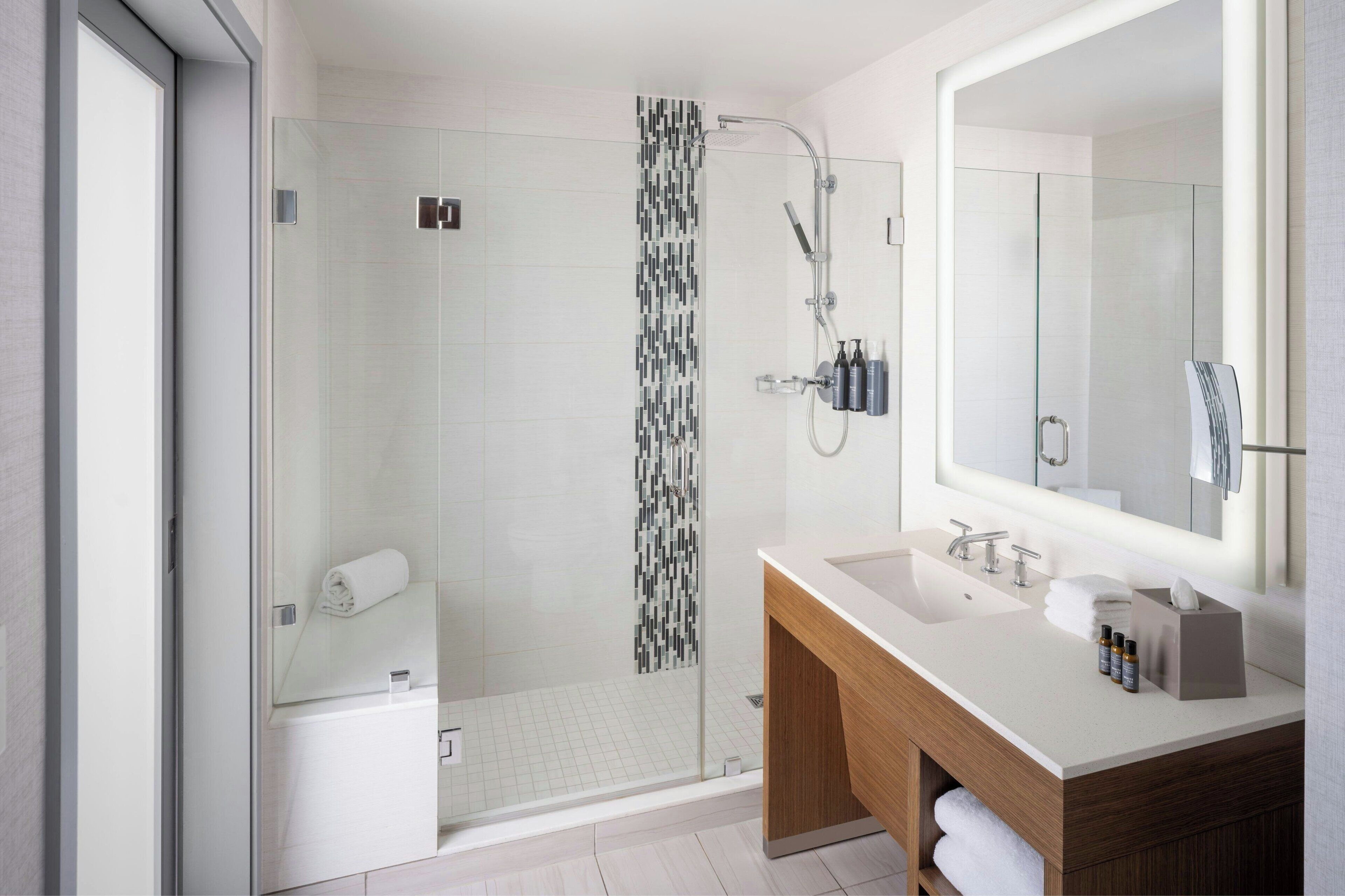 A modern bathroom with a glass-enclosed shower, a large mirror, and a wooden vanity.