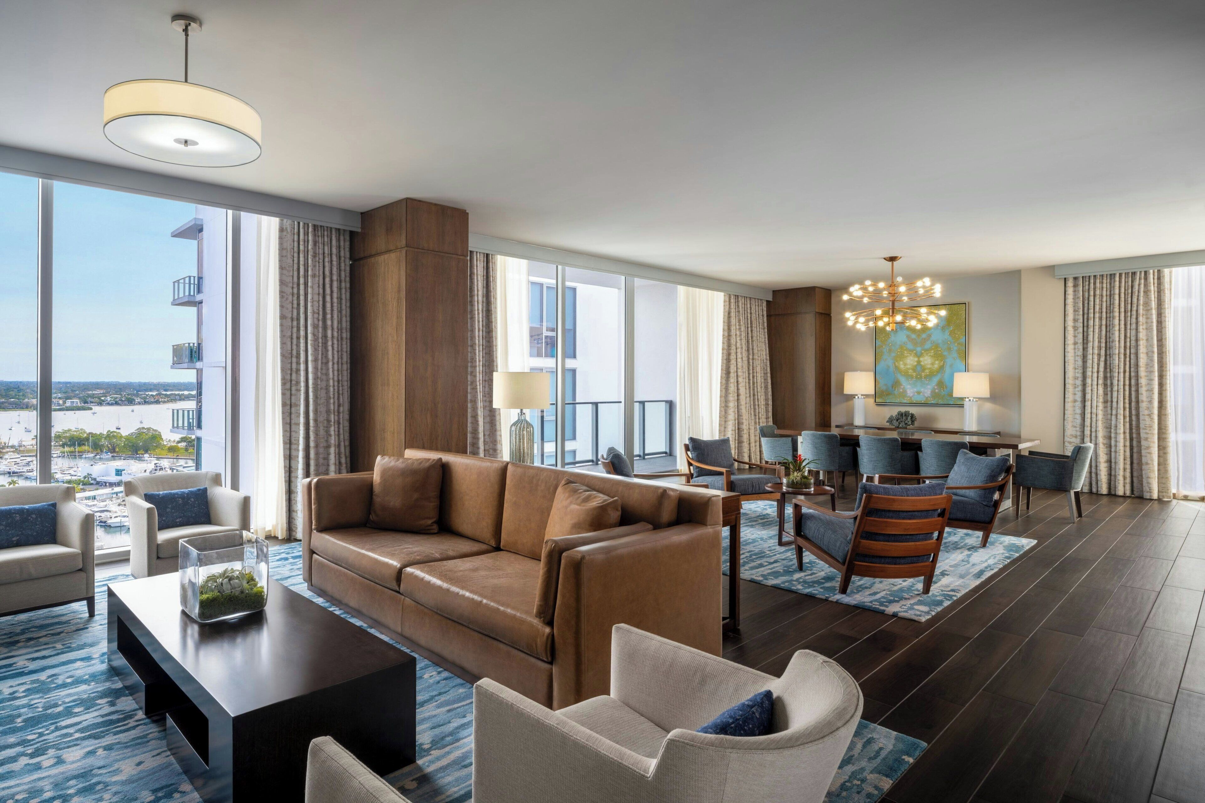 Et moderne hotelværelse med stort vindue, sofa, spiseplads og lysekrone.