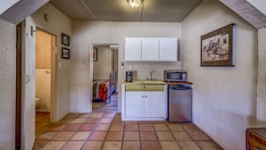 Cocina compacta con armarios blancos, un lavamanos, un microondas y un refrigerador pequeño.