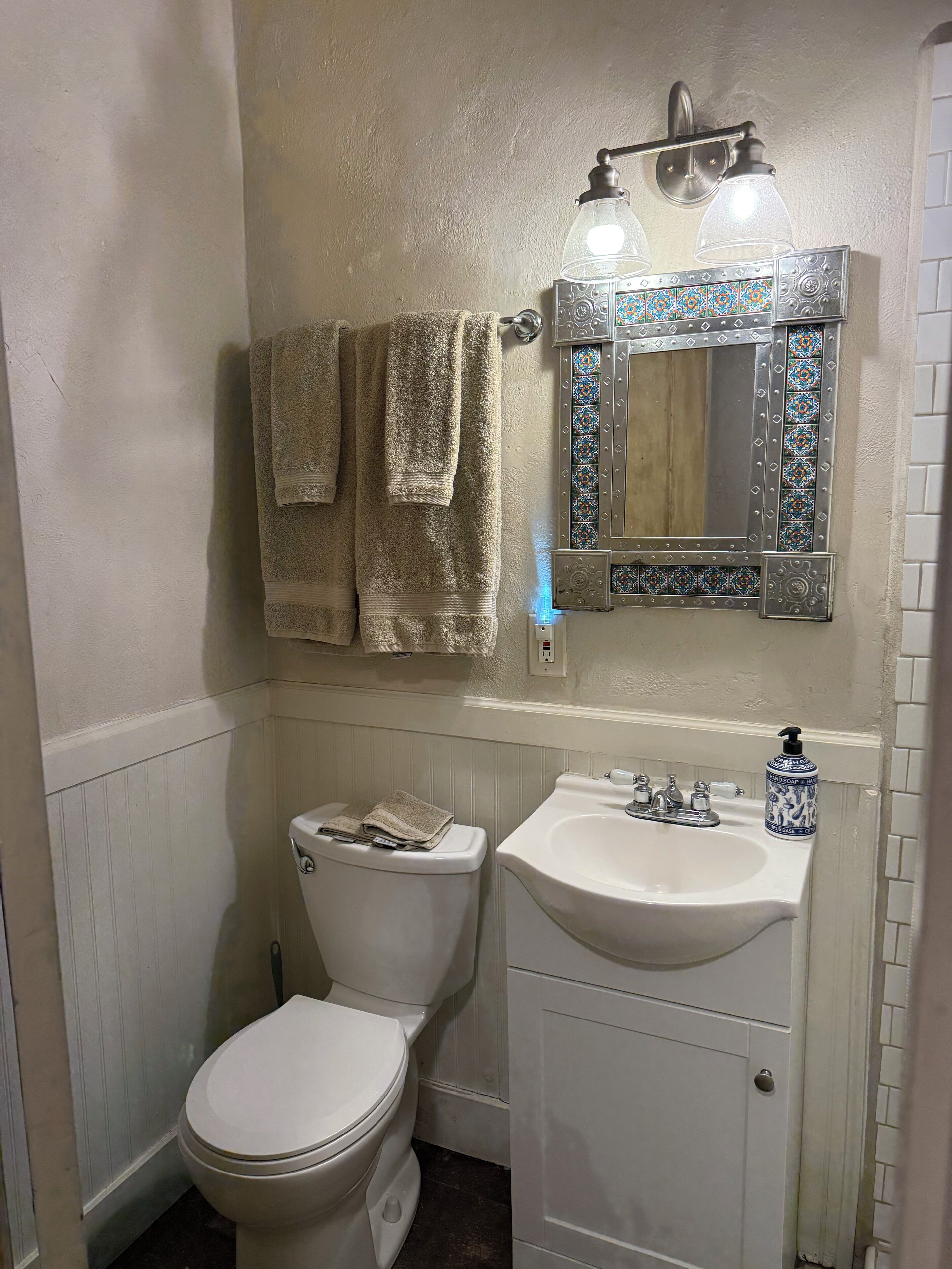 Un baño con inodoro, lavabo y espejo con azulejos decorativos.