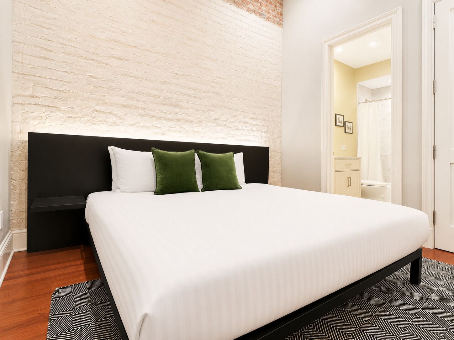 Habitació d'hotel amb un llit gran, una paret decorativa de maó, un capçal de llit negre i una catifa bicolor negre i blanc.