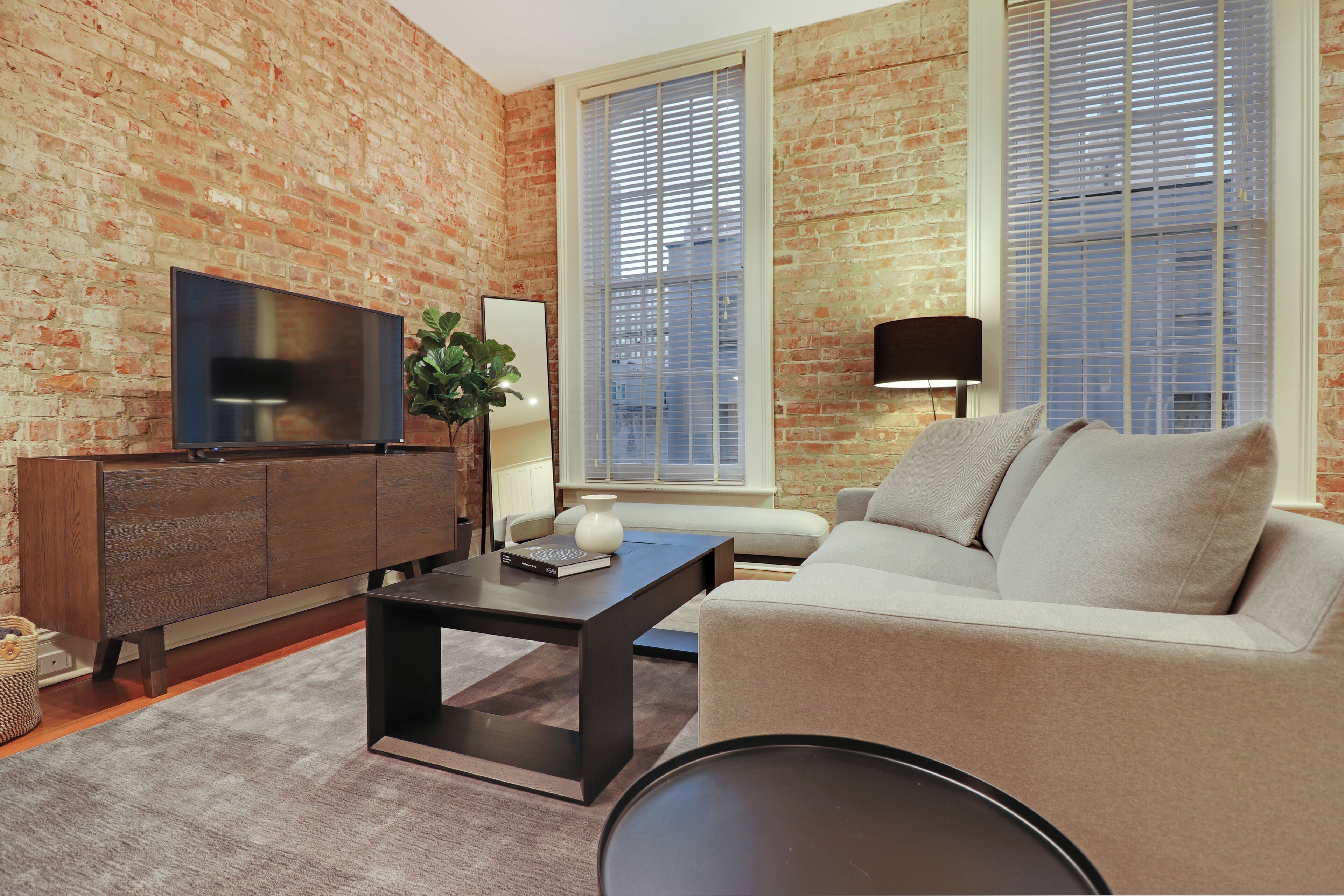 A living room with a brick wall, a flat-screen TV, a sofa, a coffee table, and a lamp.