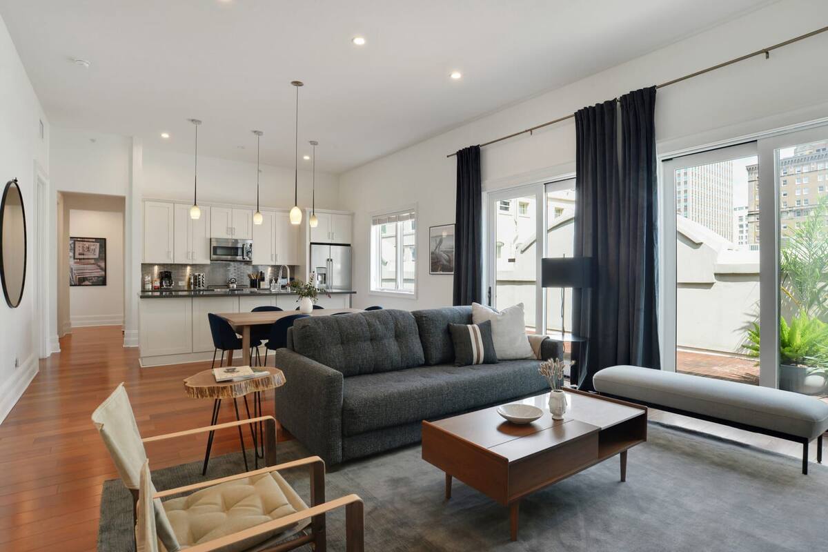 Um apartamento moderno com sala de estar, área de jantar e cozinha. Há uma janela grande com cortinas, um sofá, uma mesa de centro e uma mesa de jantar.
