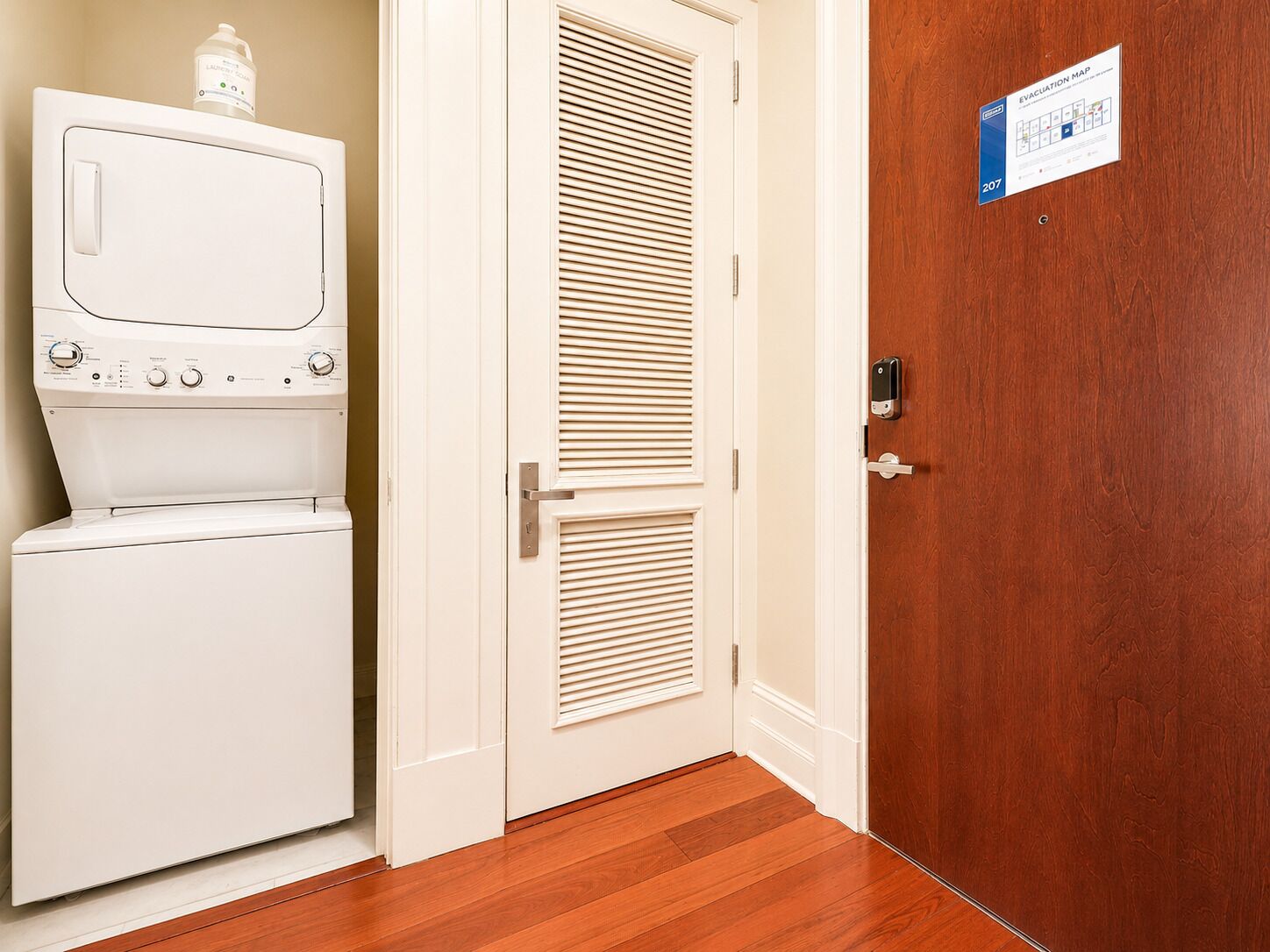 A laundry room with a washer and dryer, a door with a peephole, and an evacuation map on the wall.