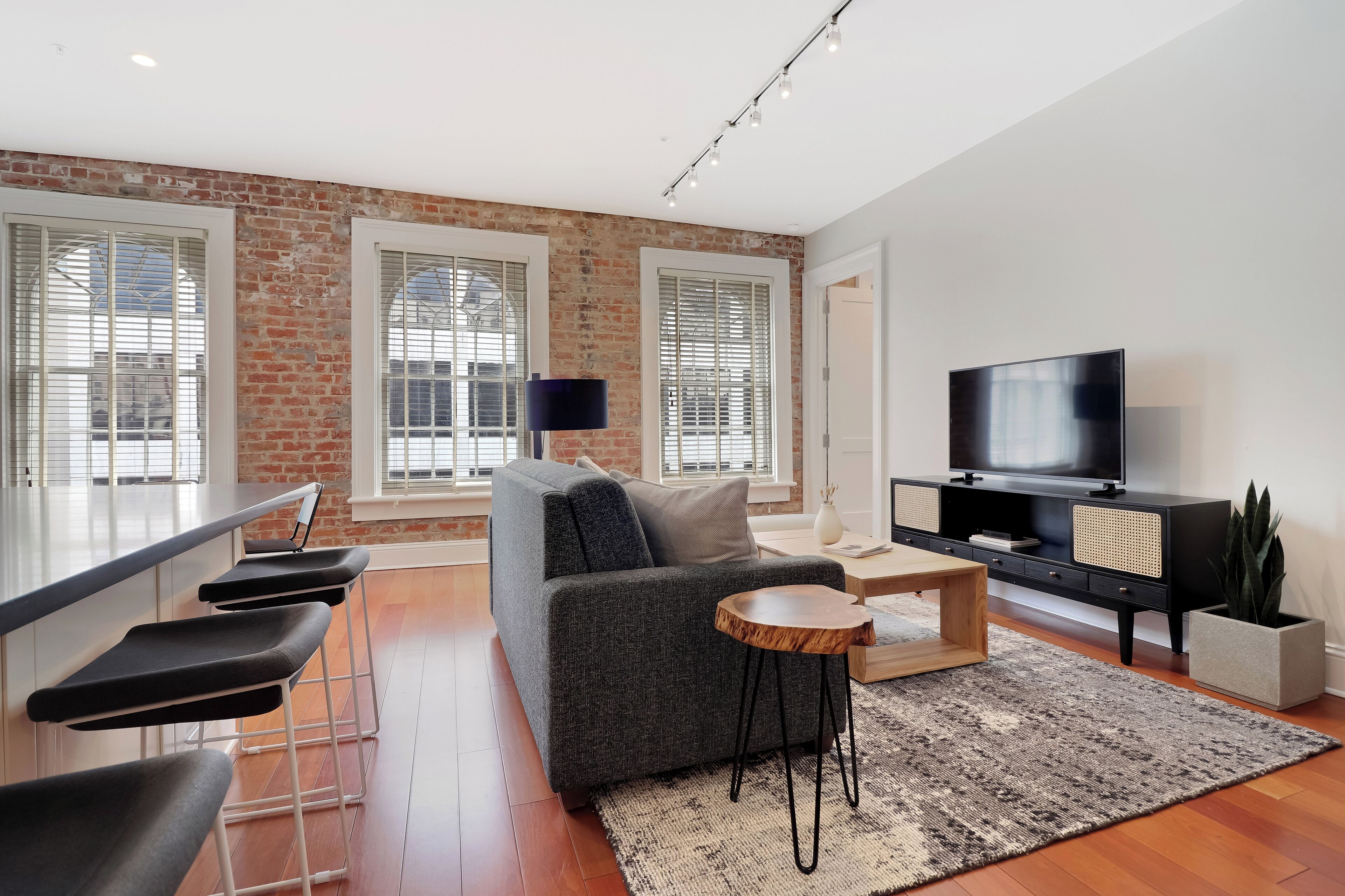 Una sala de estar moderna con un sofá gris, un televisor, un mueble de entretenimiento negro y una zona de bar con taburetes.