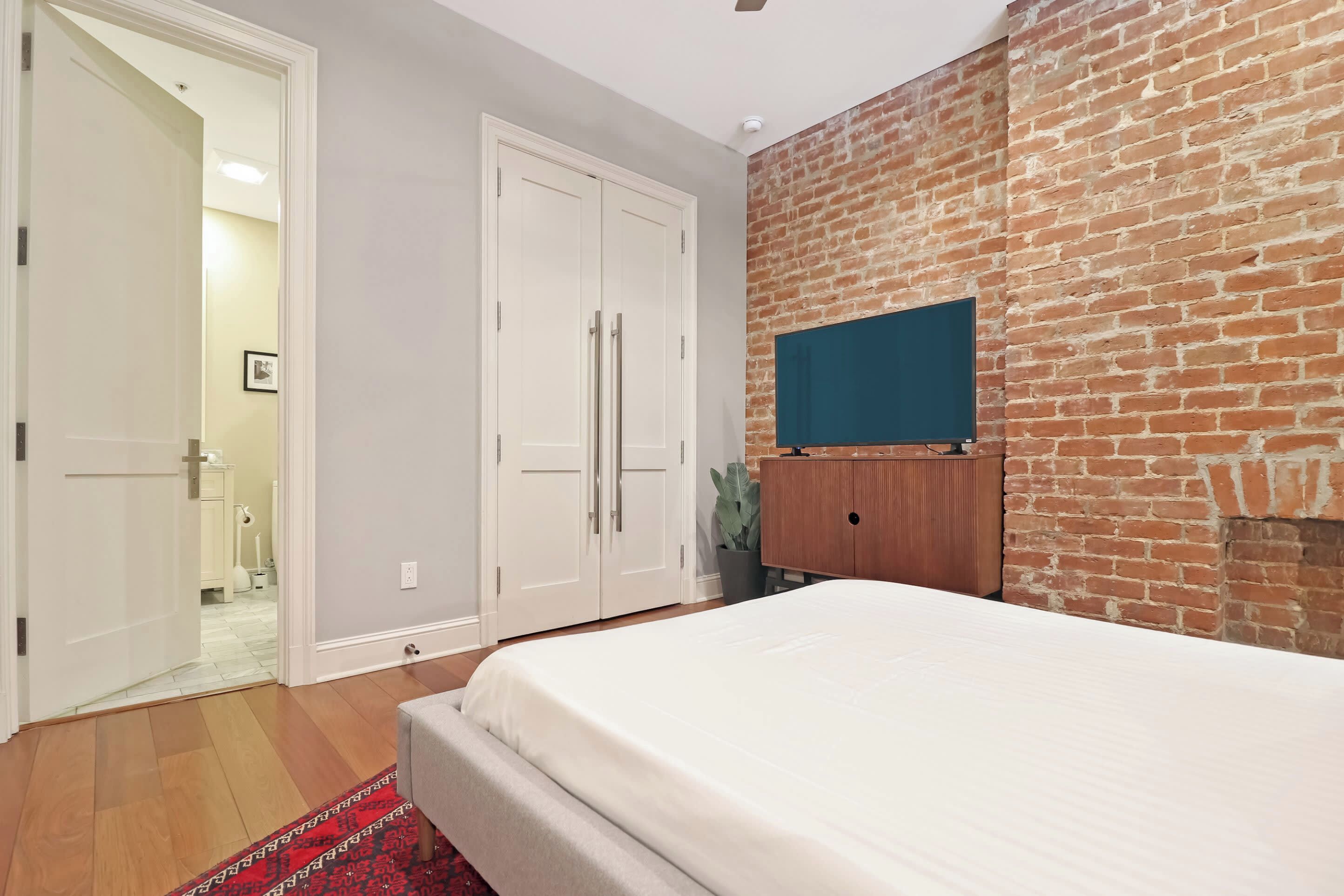Un dormitorio con cama, armario, pared de ladrillo y televisor.