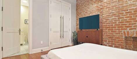 Un dormitorio con cama, armario, pared de ladrillo y televisor.