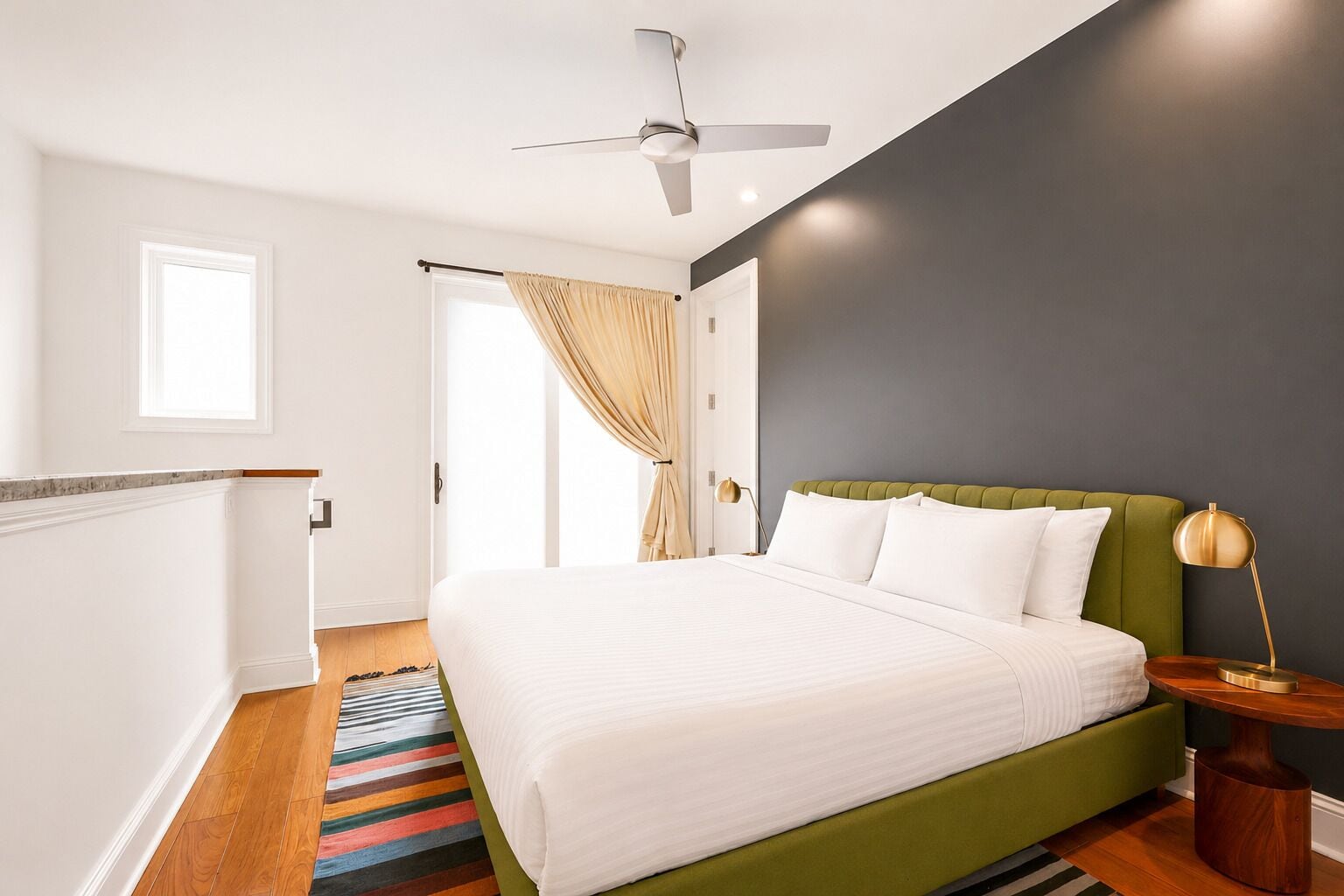 Une chambre à coucher avec un lit, un ventilateur de plafond, une table de chevet, une lampe et une fenêtre avec des rideaux.