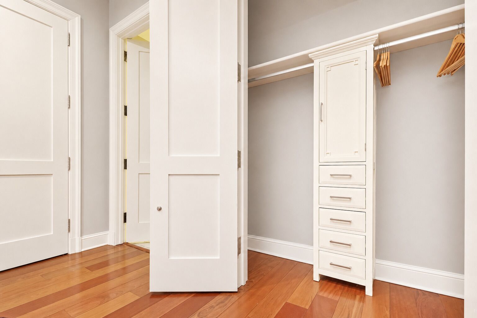 Ein begehbarer Kleiderschrank mit Holzboden, weißen Türen und einer eingebauten Garderobe mit mehreren Schubladen.