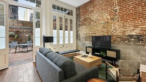 A modern living room with a grey sofa, a wooden coffee table, a TV, and a brick wall. - Roami at Factors Row (New Orleans)