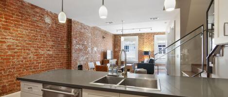 Una cocina moderna con pared de ladrillo, electrodomésticos de acero inoxidable e iluminación colgante.