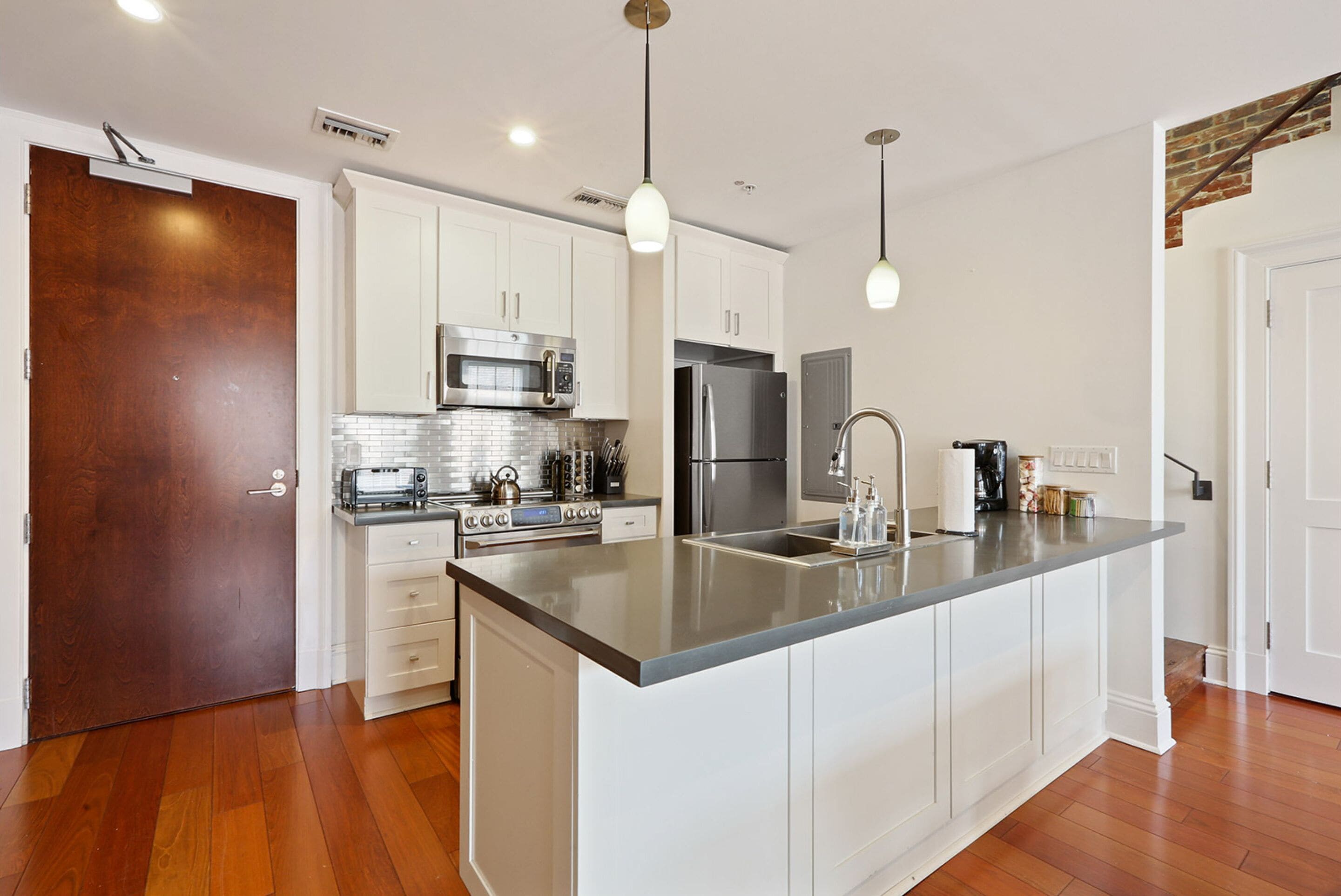 Una cocina moderna con armarios blancos, electrodomésticos de acero inoxidable y una isla grande con encimera gris.