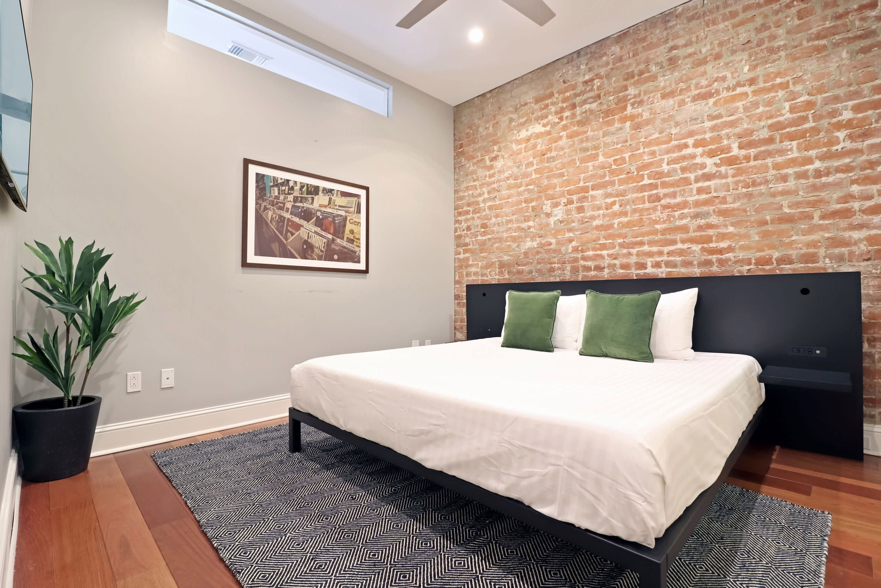 Un dormitorio moderno con pared de ladrillo, una cama grande con ropa blanca y una planta en maceta.