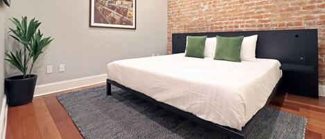 Un dormitorio moderno con pared de ladrillo, una cama grande con ropa blanca y una planta en maceta.