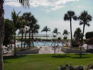 A pool area with palm trees, a view of the ocean, and a beach in the background.