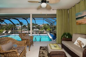 Uma área à beira da piscina com móveis de vime, um sofá e um ventilador de teto.