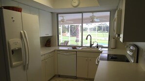 Eine Küche mit Kühlschrank, Spüle und Fenster mit Blick auf eine Rasenfläche.